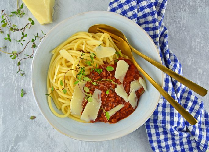 Opskrift vegetar spaghetti bolognaise pyntet med parmesanflager i en tallerken med ske og gaffel