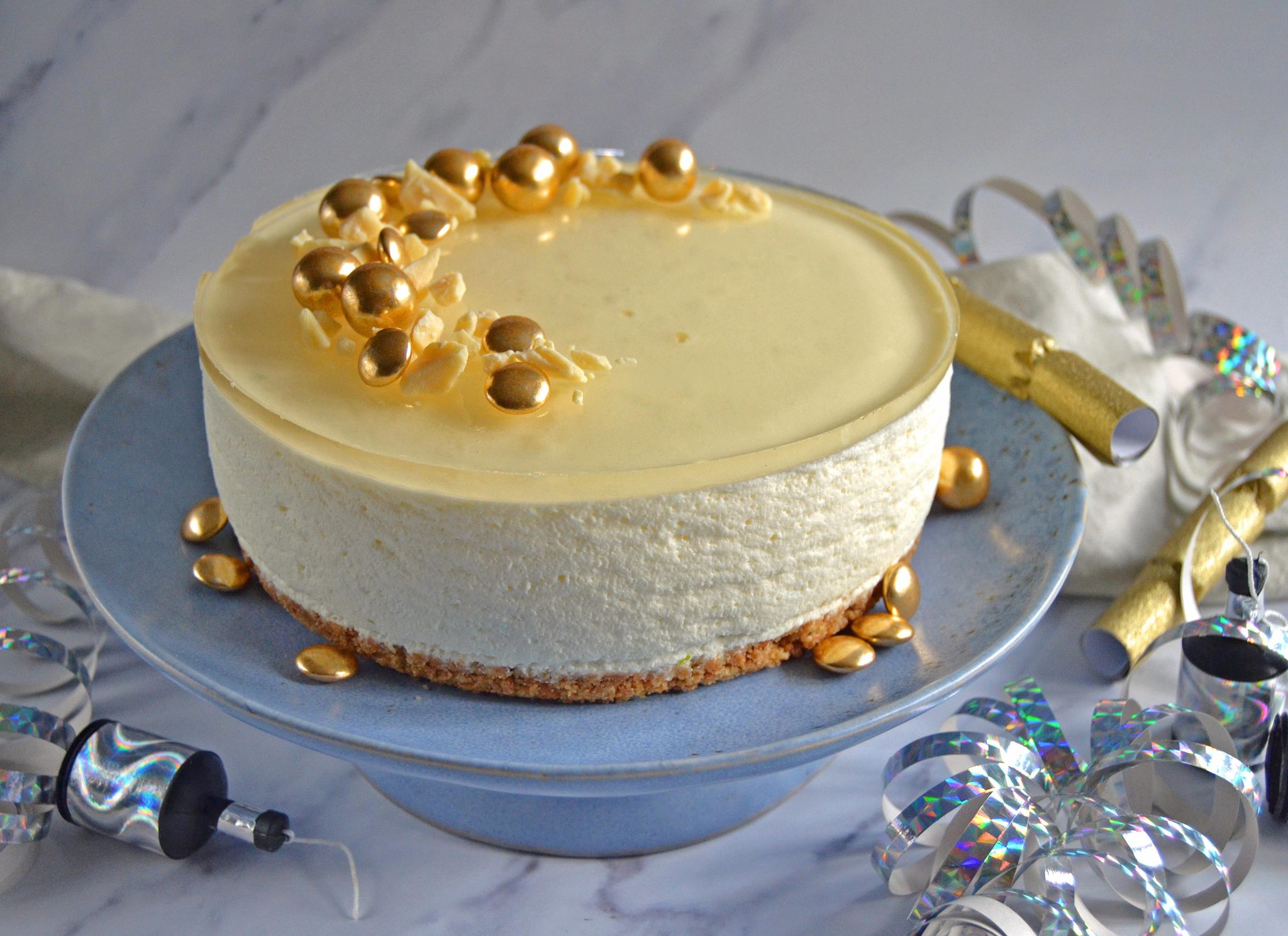 Opskrift nytårs cheesecake med astigelé og guldpynt på et blåt fad pyntet med serpentiner og knallerter
