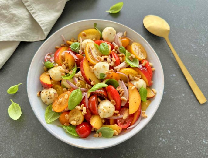 Opskrift nektarinsalat med tomater og mozzarella i en skål - pyntet med frisk basilikum og pinjekerner