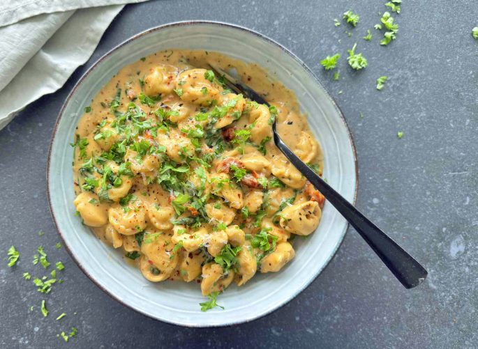 Opskrift one pot tortellini med spinat og flødesauce anrettet i en skål med et drys persille