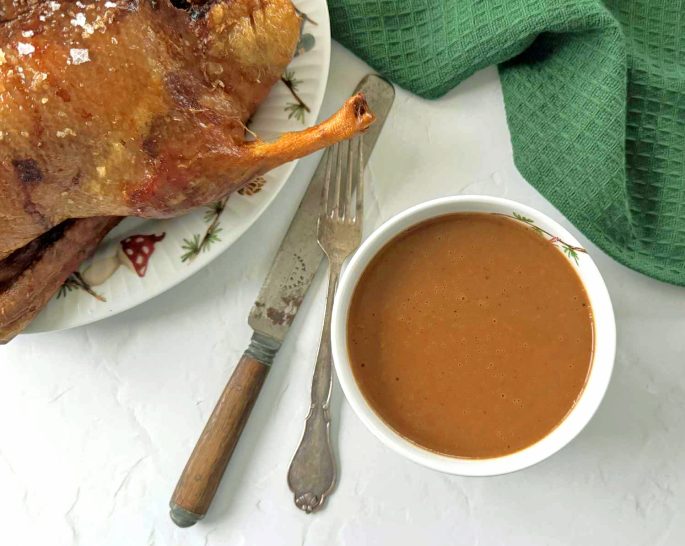 Opskrift brun andesauce i en skål ved siden af en andesteg - lækker opskrift på julesauce