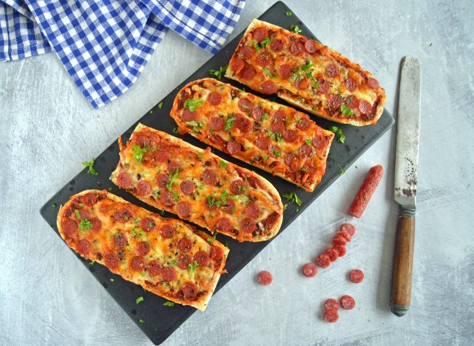 Opskrift på pizza baguettes med mini pepperoni, anrettet på et fad med et blåt og hvidt viskestykke